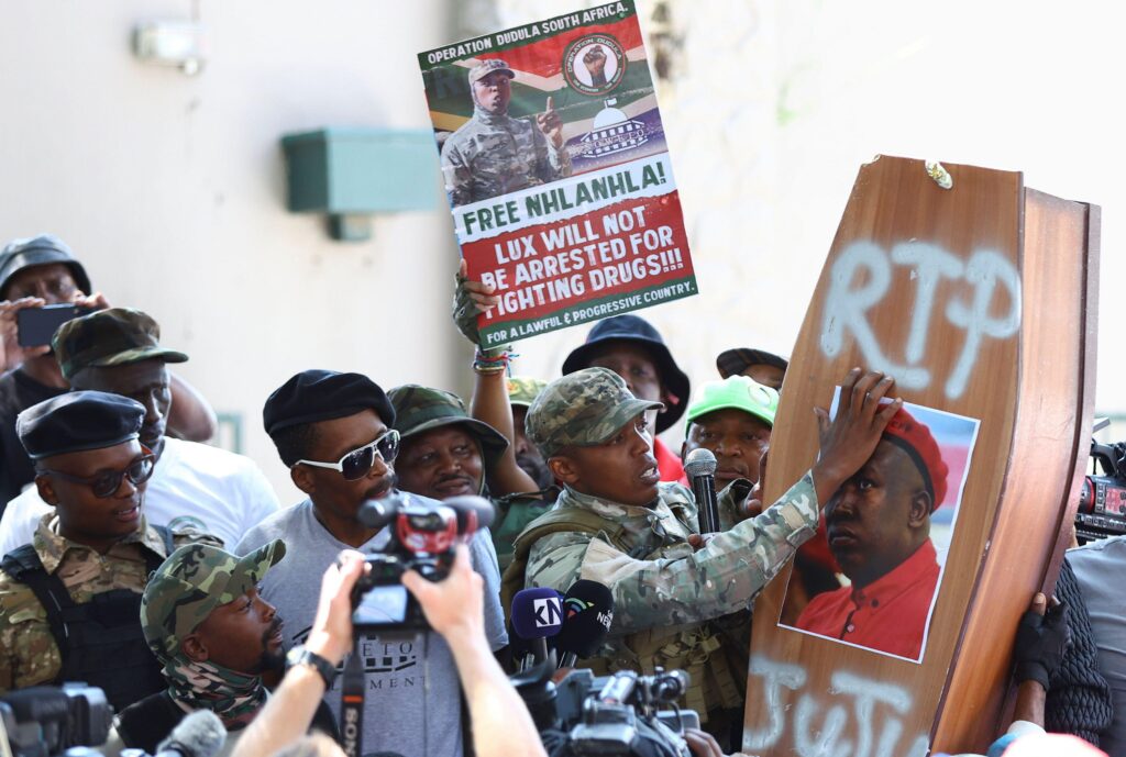 The leader of Operation Dudula, Nhlanhla "Lux" Dlamini, wearing paramilitary-style camouflage gear rip a picture bearing Economic Freedom Fighters (EFF) leader Julius Malema, which was stuck onto a coffin, during his address to supporters outside the magi